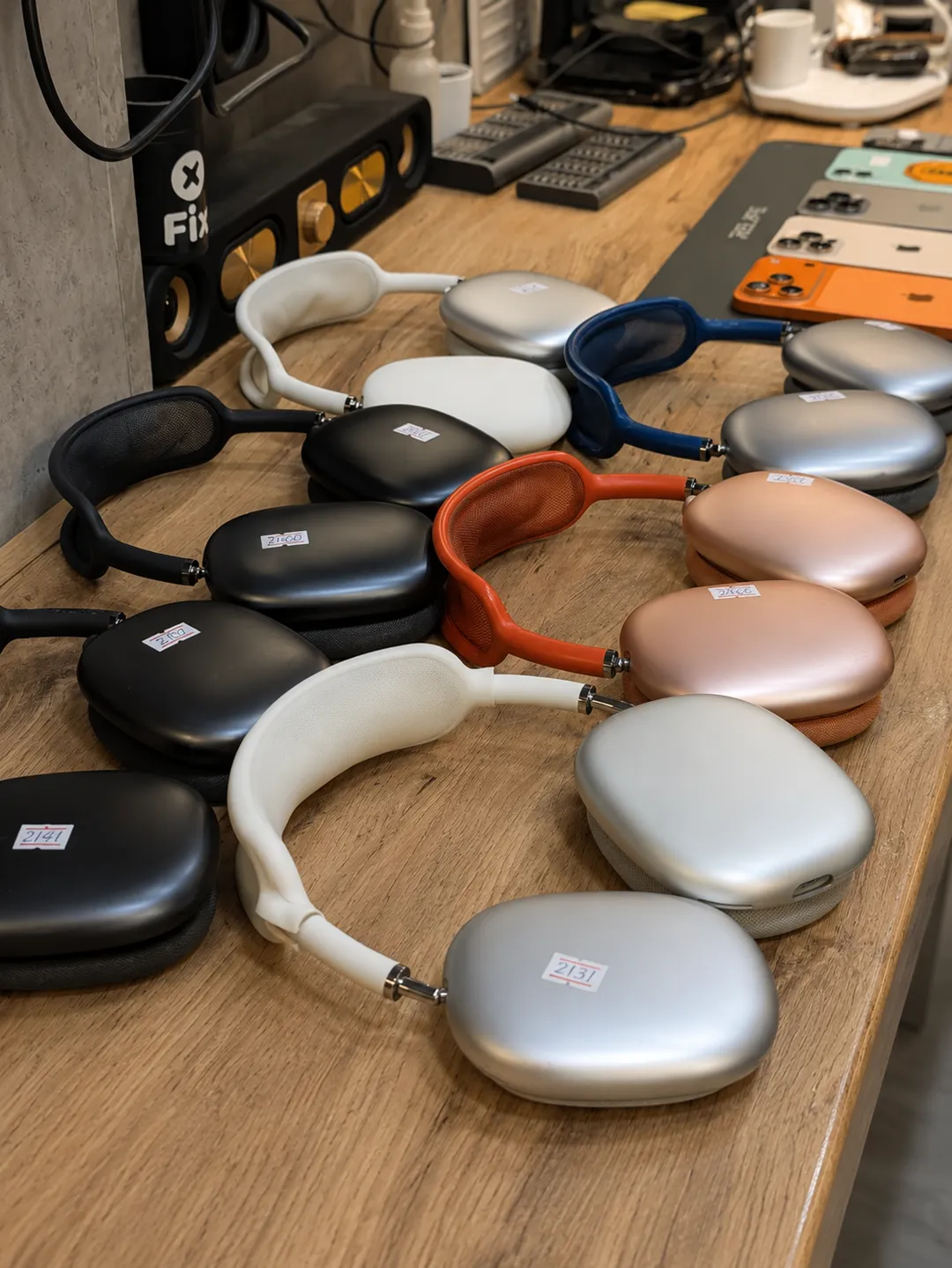 AirPods Max headphones with repair tickets, lined up on a workbench