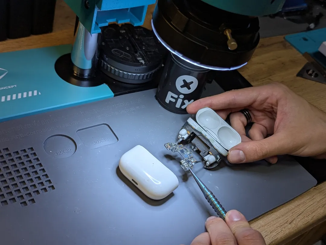 AirPods Pro case opened under the microscope, its board held with tweezers