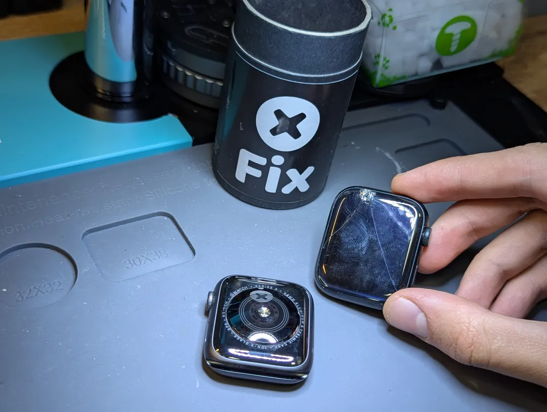 Cracked Apple Watch screen held next to the watch, on an anti-static mat