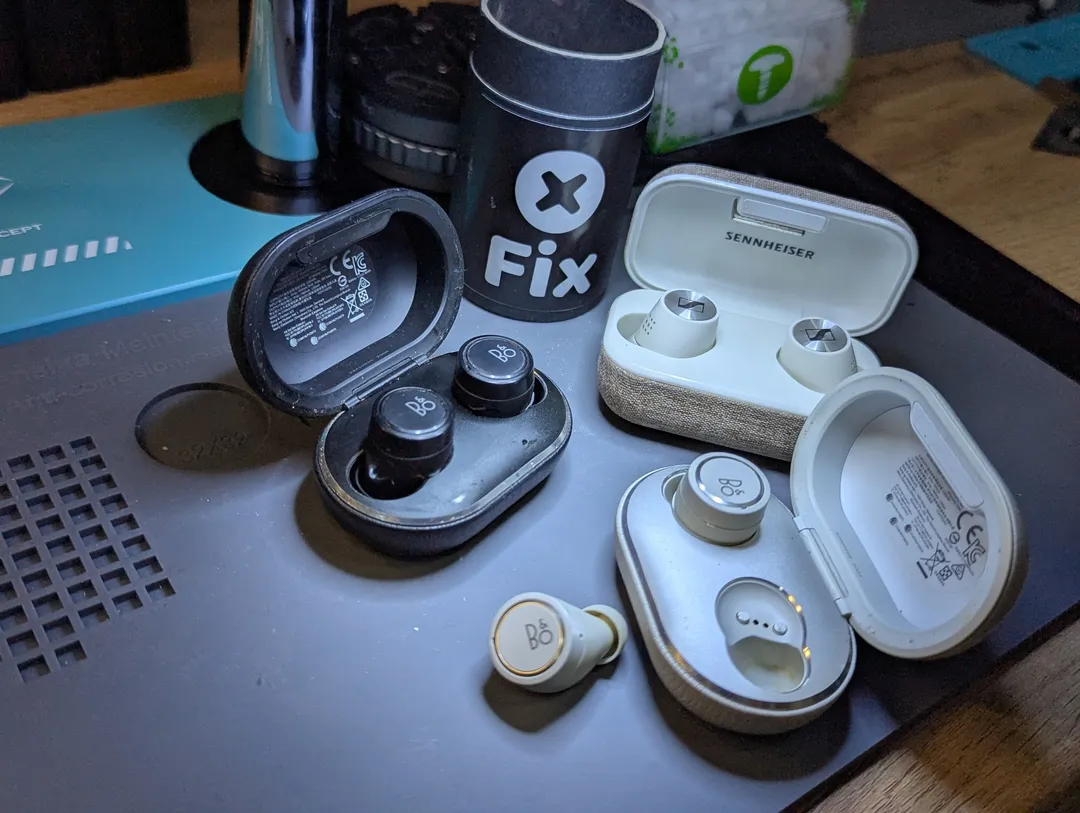 Bang & Olufsen and Sennheiser earbuds with their cases, on an anti-static mat