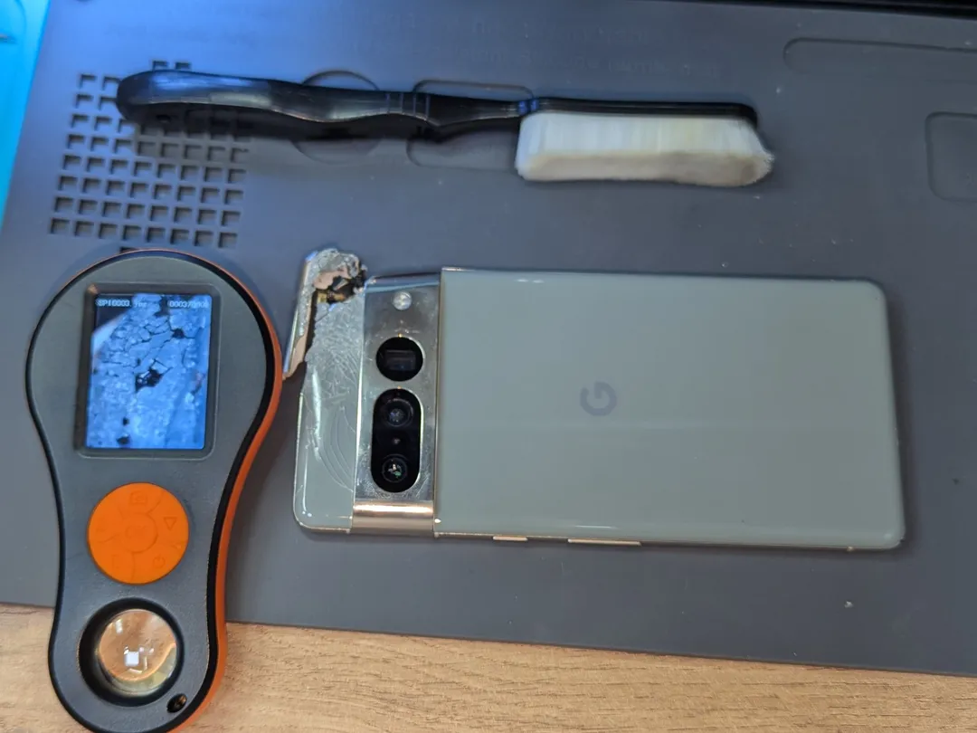 Google Pixel 7 Pro with shattered back glass on an anti-static mat, next to a digital magnifier