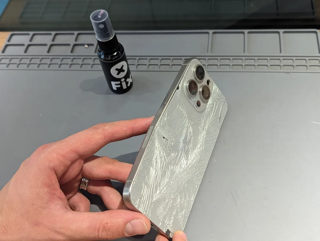 iPhone Pro with shattered back glass, held over an anti-static mat
