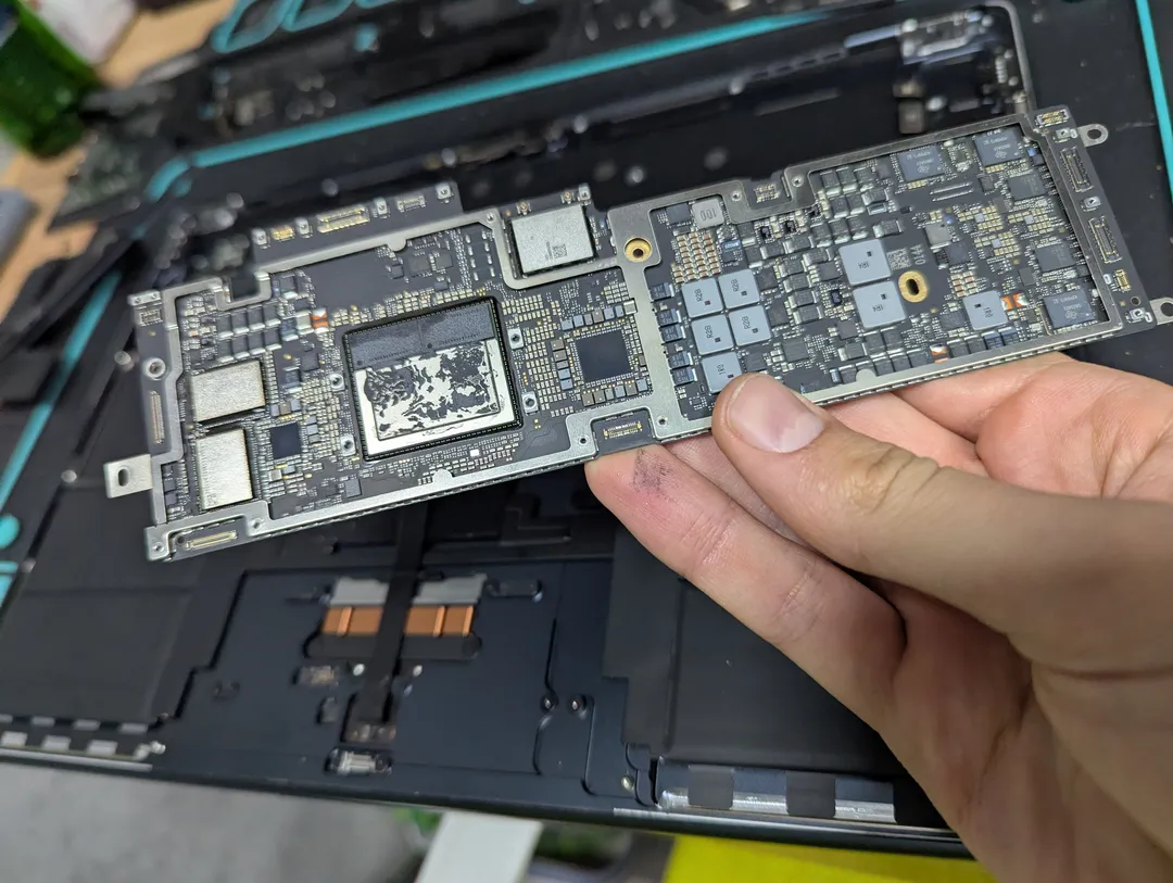 MacBook Air logic board taken out of the laptop, held over the opened case