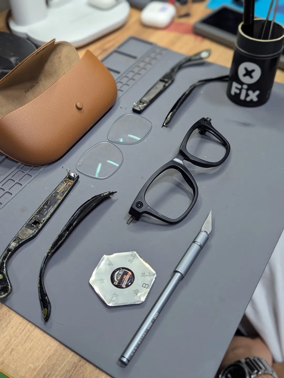 Ray-Ban Meta glasses taken apart on an anti-static mat: frame, lenses and opened arms, next to the charging case