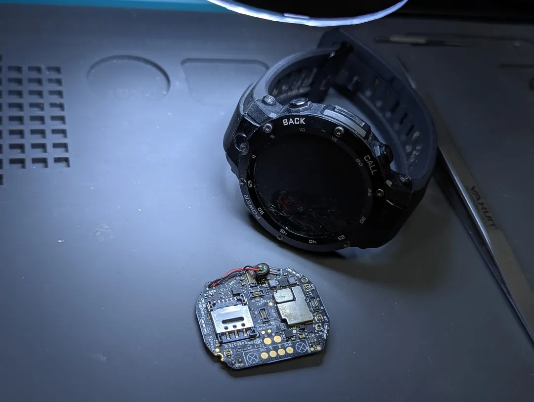 A rugged smartwatch taken apart on an anti-static mat, its board beside it