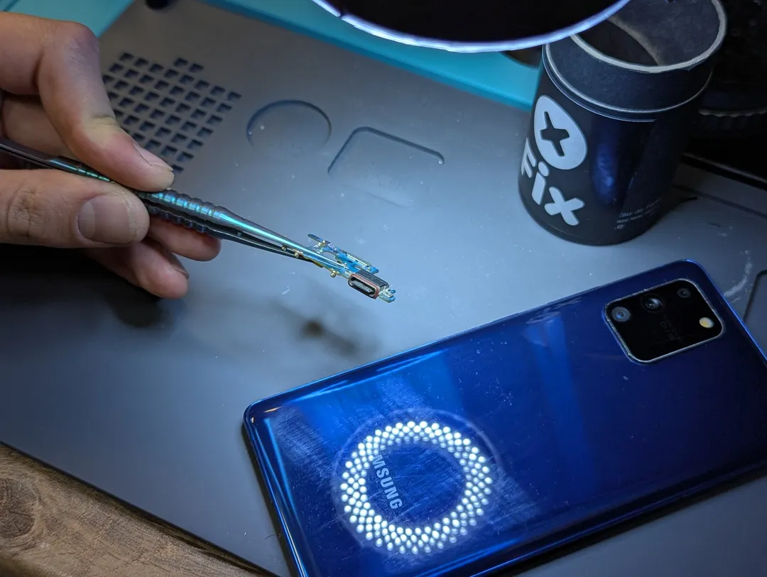 Плата разъёма зарядки в пинцете рядом с Samsung Galaxy